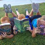 3 children lying in grass, reading