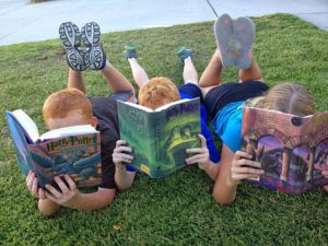 3 children lying on grass, reading