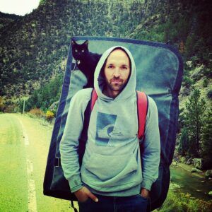 Man with backpack; black cat on shoulder