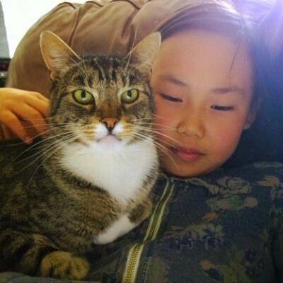 Young girl holding tabby cat, white vest